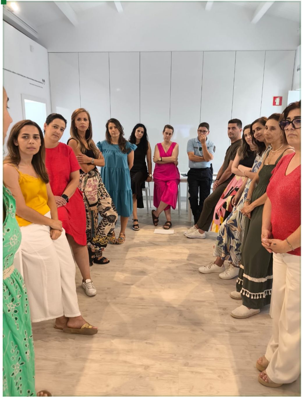 cerca de 15 homens e mulheres estão de pé a formar um circulo para ouvir a formadora